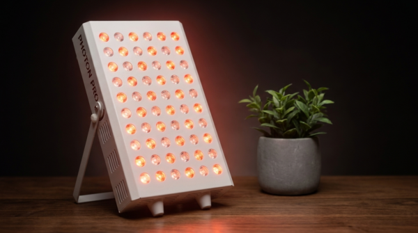 Kompaktes Photon Panel M mit 60 LEDs steht auf seinem Klappständer auf einem dunklen Holztisch und leuchtet warm rot