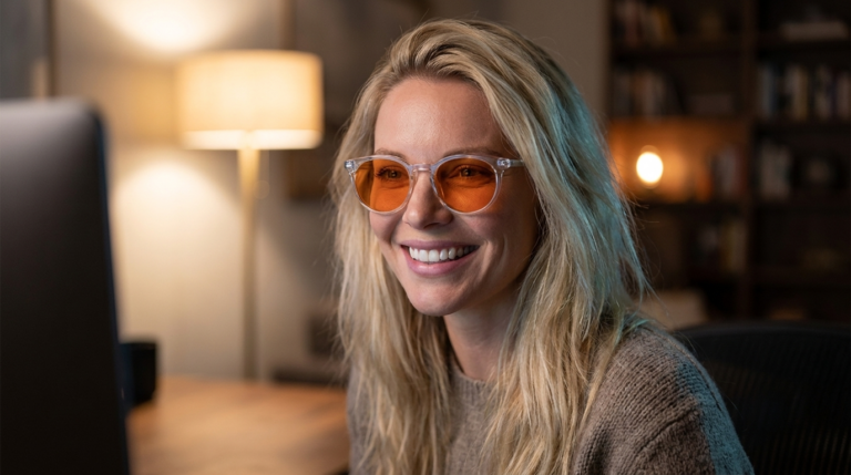 Frau am Schreibtisch trägt eine runde Blueblocker-Brille mit klarem Rahmen und orange getönten Gläsern