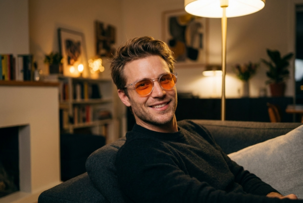 Junger Mann mit orange getönter Houston Blaulichtfilter-Brille lächelt entspannt abends auf dem Sofa